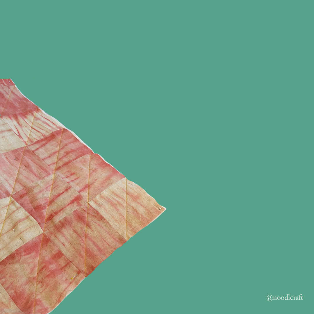 A triangular view of the first piece of quilted fabric. Diagonal stitches are done across the square pieces.