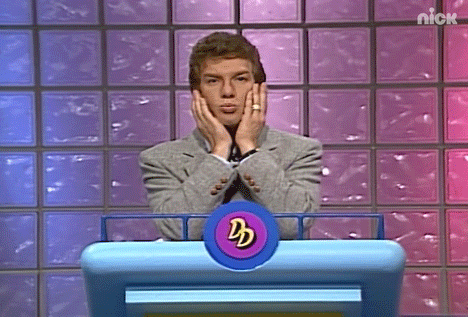 A man in a suit standing at a podium making a funny expression while tapping his fingers on his face