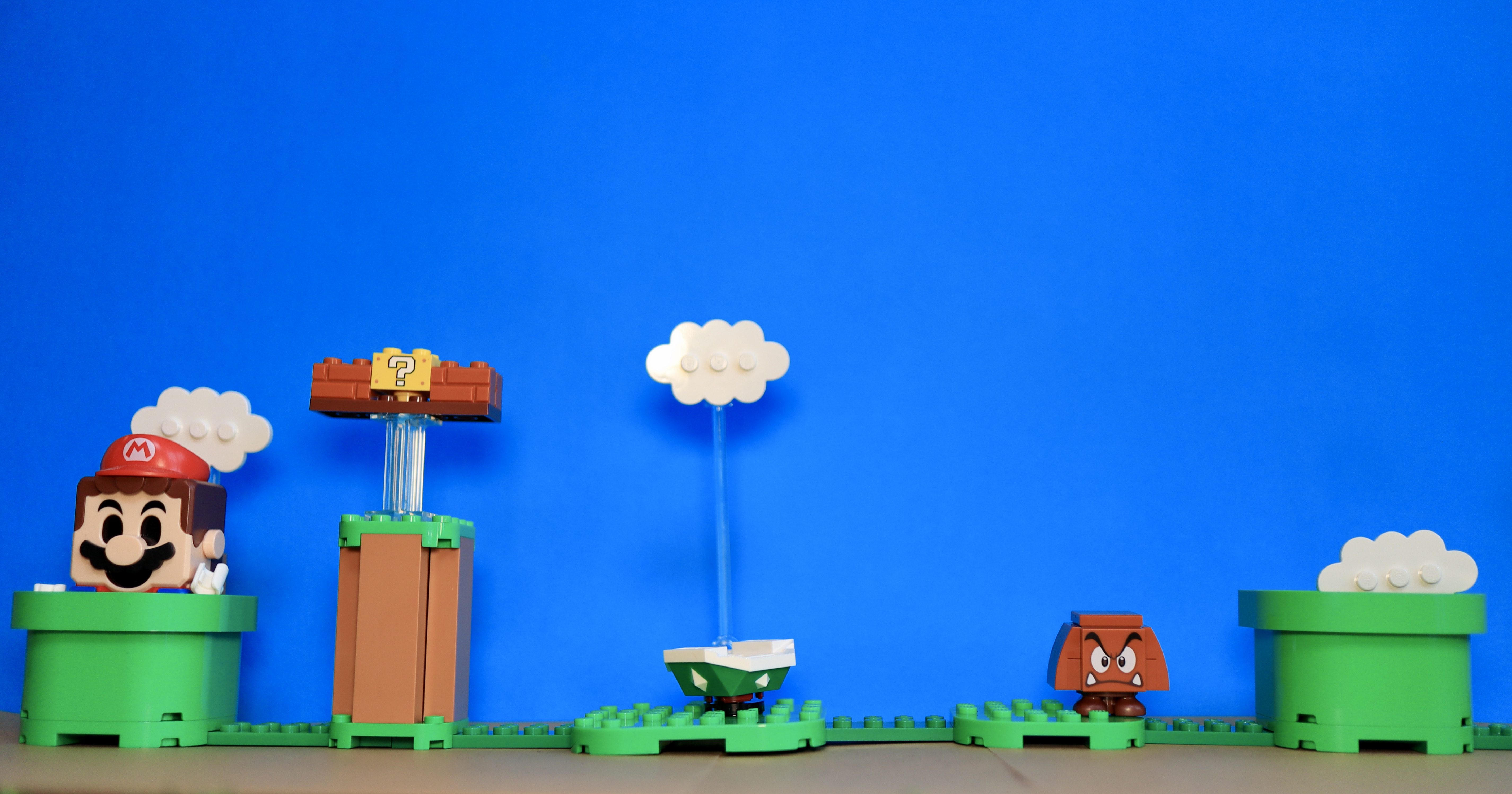 Lego Super Mario Bros with Mario emerging from a pipe, a 1UP being triggered, a goomba under a cloud, and a cloud emerging from another pipe.