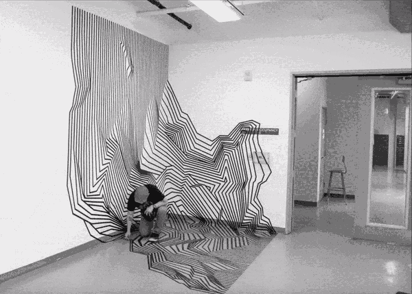 Un timelapse de Darel Carey con gorra y camiseta negra cologando cinta aislante del suelo a la pared en una habitación vacía y blanca. Distintas líneas de cinta van realizando formas angulosas y la siguiente varia ligeramente en ancho y distnancia creando la percepción de que hay una forma tridimensional pese a no usar ningún tipo de sombra o tinta.