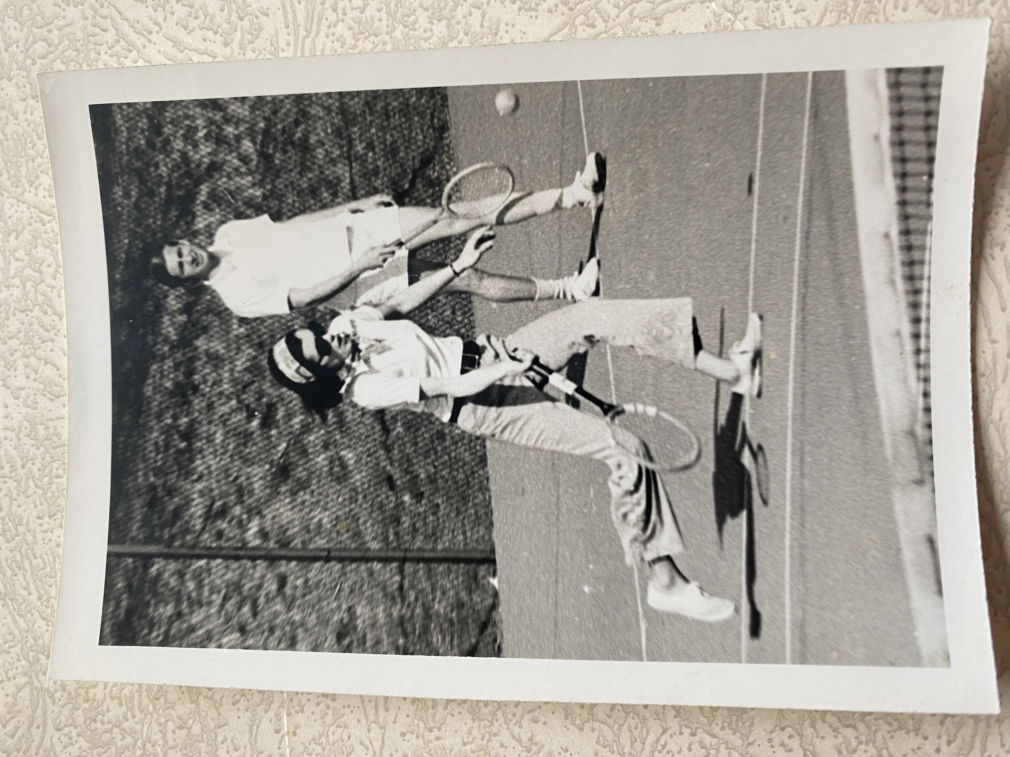 A black and white photo from the 1960s of a woman with a tennis racket extended, about to hit the ball