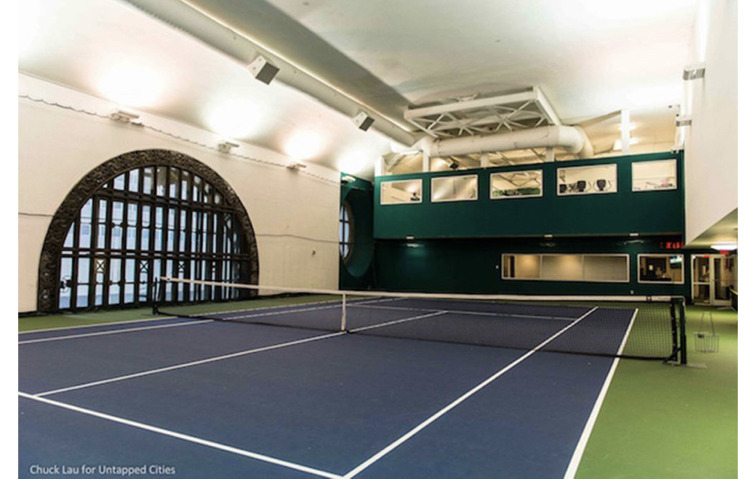 An empty tennis court with a large arching window on the side wall