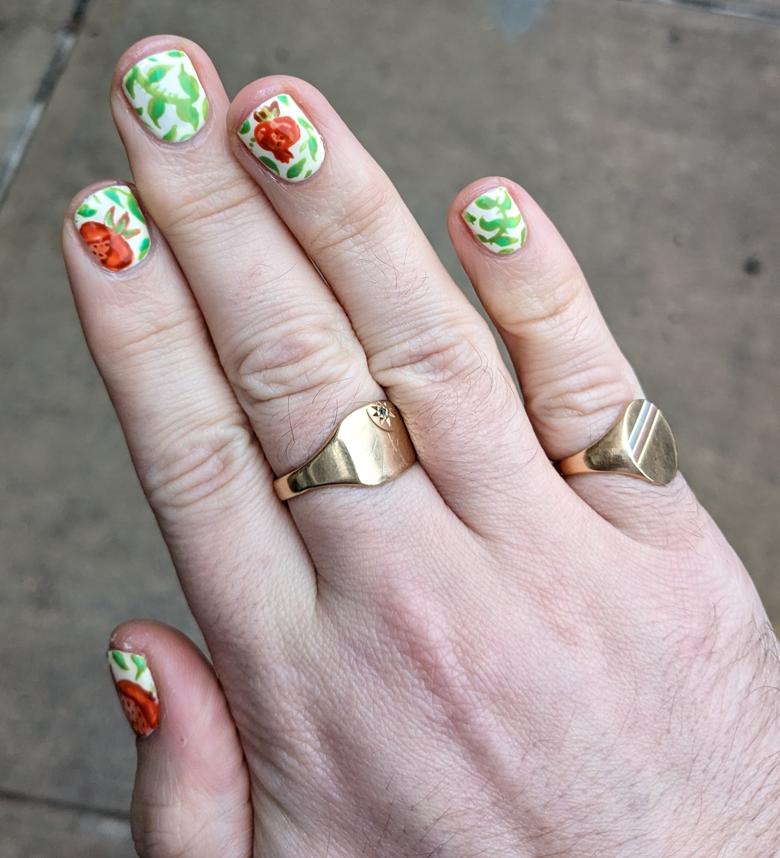 A hand with nails painted with pomegranates.