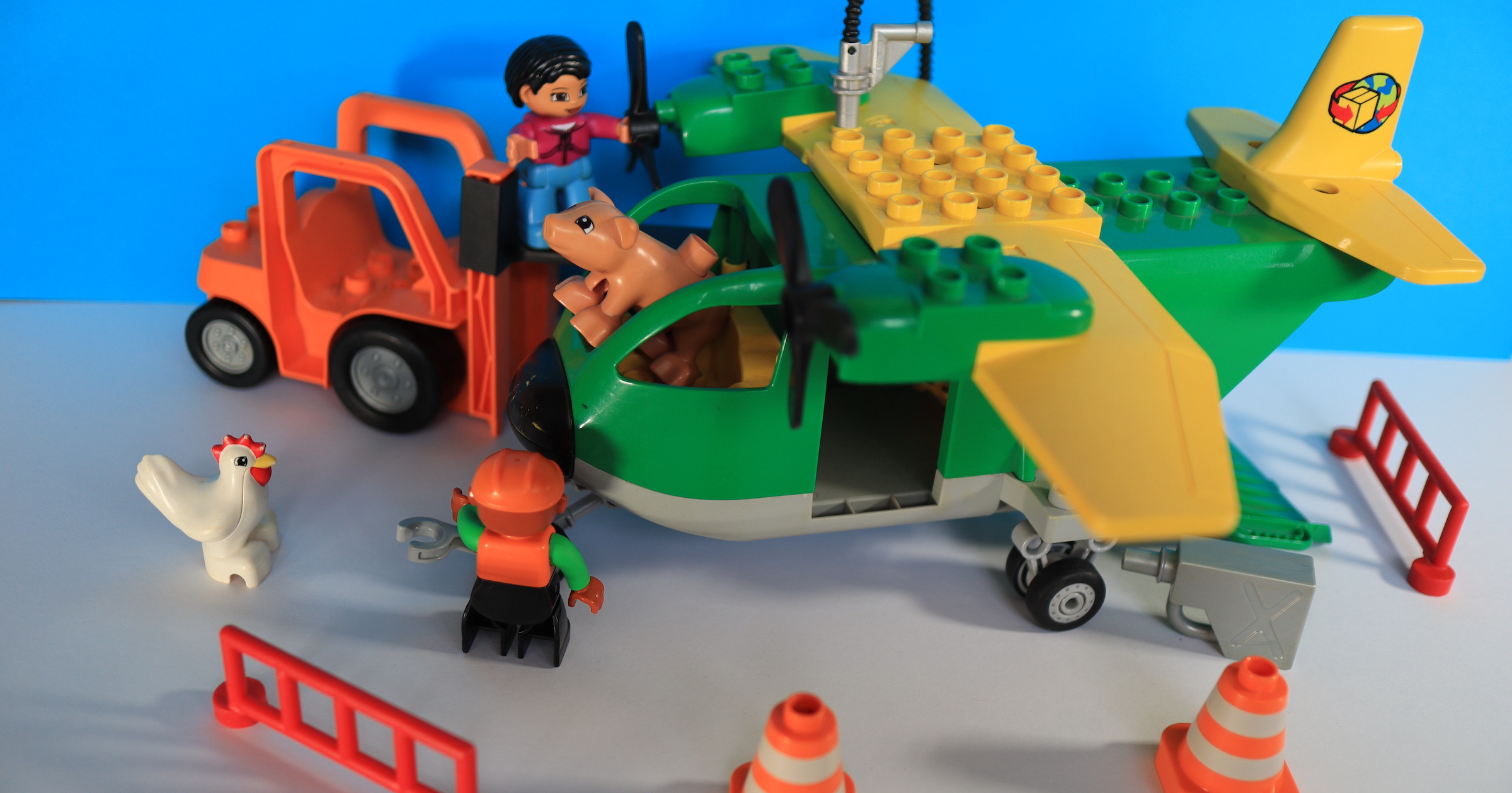 Photograph of a Duplo aeroplane with two technicians performing maintenance work. The plane is flown by a pig. A chicken is watching the workers. Safety barriers protect the worksite.