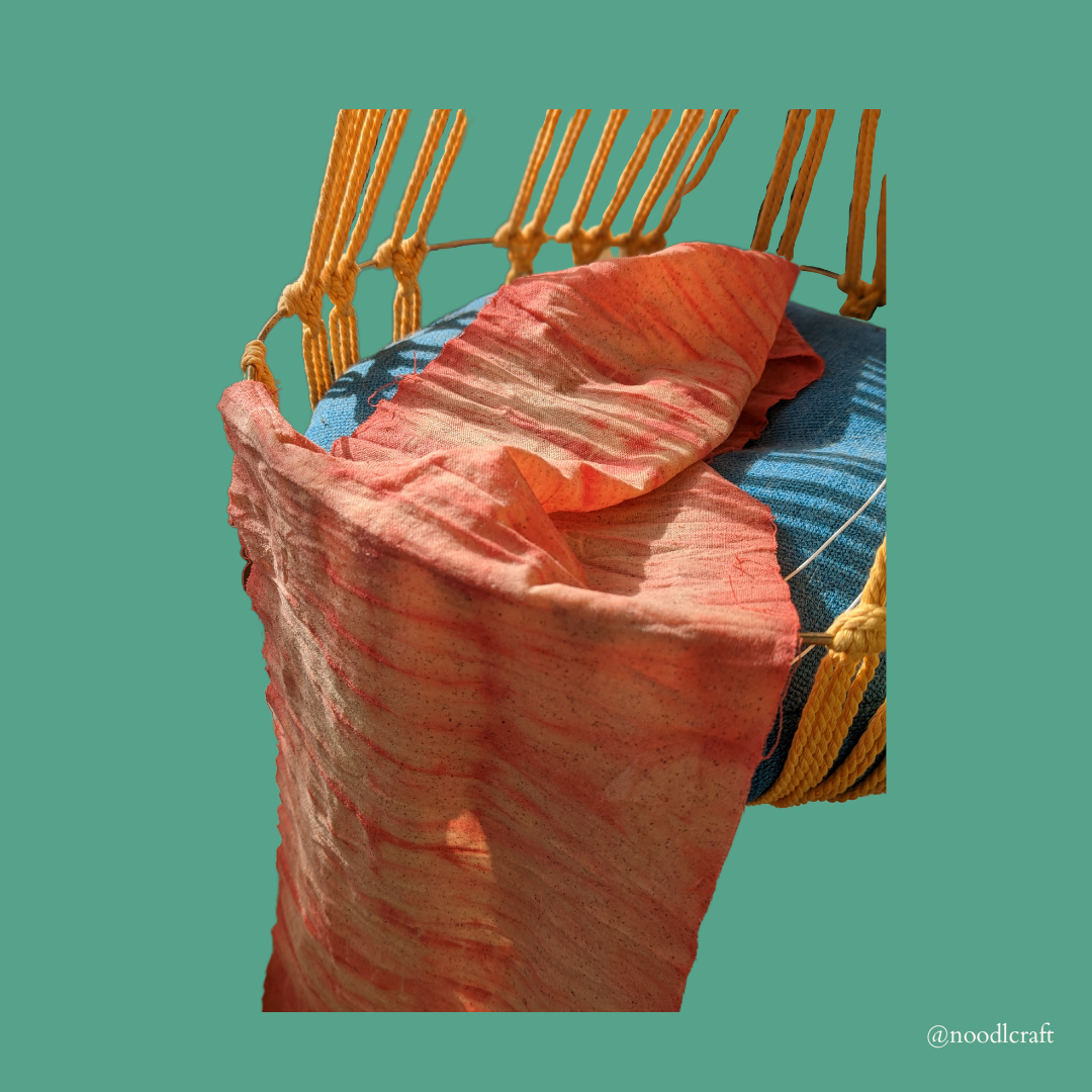 A piece of pink-dyed fabric hanging on on macramé cat bed.