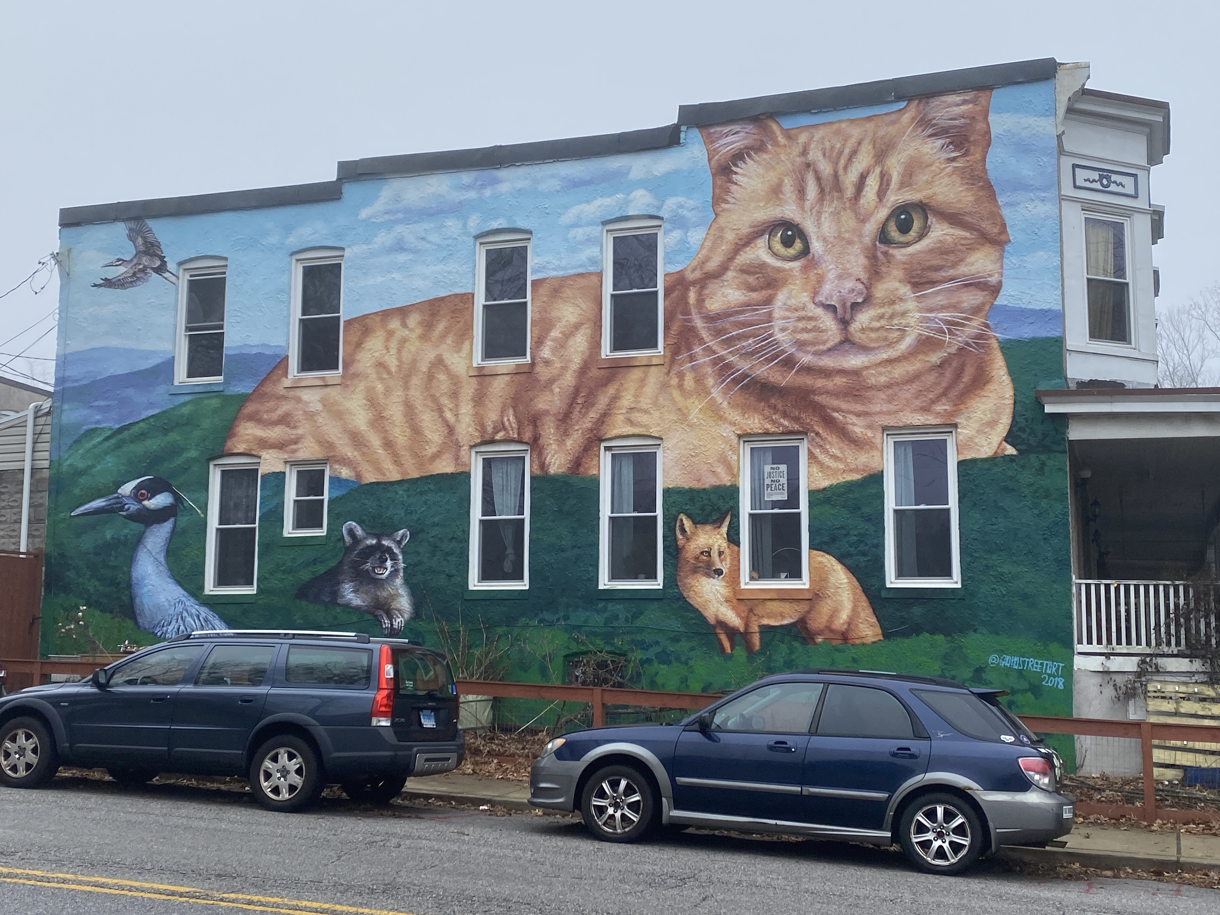 The side of a house or apartment building covered in a mural of a large cat and other wildlife
